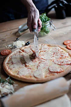 Male hands are cooking pizza with sausage and ingredient on the wooden table in rustik style