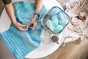 Male hands crochet handmade artwork use wool yarn and hook over table with coffee