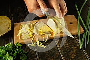 Male hands cut fresh cabbage with a knife on a kitchen board. Low key concept for preparing a diet salad at home