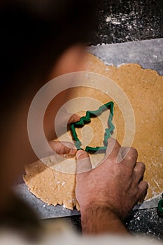 Male hands cut out gingerbread cookie in the form of a snowflake, Christmas tree, a man from raw dough on parchment baking paper