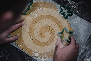 Male hands cut out gingerbread cookie in the form of a snowflake, Christmas tree, a man from raw dough on parchment baking paper