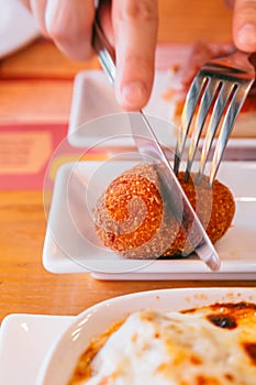 Male hands cutting Papas Rellenas the most popular type of croquettes in Latin American countries with knife and fork photo