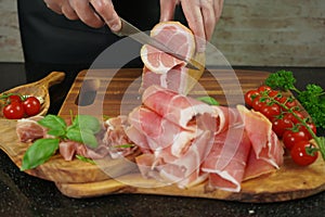 Male hands cutting with sharp knife traditional Spanish dry smoked ham leg