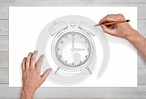 Male hands drawing a retro alarm block with two bells using a pencil on a white paper in close view.