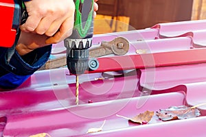 Male hands drill a hole in the roof for the screw with a screwdriver. Roof repair