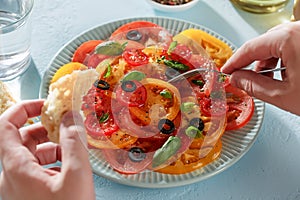 Male hands eat tomato salad with piece of bread with a fork.