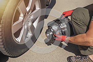 Male hands in glove and portable tire pump for inflating auto wheel. Tyre inflator air compressor with pressure gauge