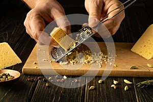 Male hands grate hard milk natural cheese on a cutting board with a grater before preparing a dish. Concept for making cheese