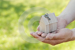 Male hands hold of cardboard house against green bokeh. Building, loan, housewarming, insurance, real estate or buying new home.