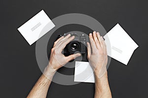 Male hands hold old vintage camera, white blank photo cards on black background top view flat lay with copy space. Concept for the