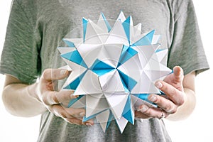 Male hands hold paper polygonal star, futuristic blue origami geometric figure.