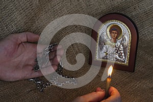 Male Hands hold a pectoral cross and a burning candle in front of a Christian icon