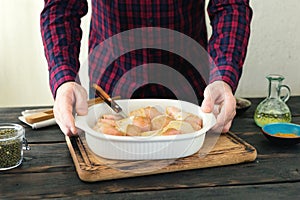 Male hands holding a baking dish with raw chicken legs