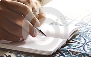 male hands holding a ballpoint pen to write on the blank pages of an open notebook