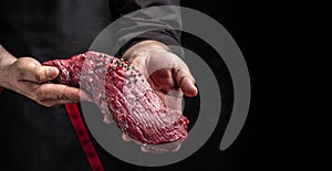 Male hands holding beef meat on a dark background, Whole piece of tenderloin with steaks and spices ready to cook, Long banner