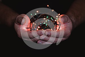 male hands holding a Christmas garland with lights on a dark background with copy space for text. Retro effect, close-up