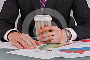 Male hands holding coffee cup with business papers on the table.