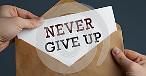 Male hands holding craft envelope with text NEVER GIVE UP on blue background