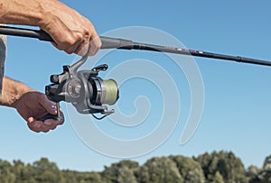 Male hands holding fishing rod or angler over blue clear sky in summer