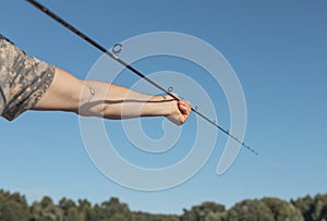 Male hands holding fishing rod and assembling it over blue clear sky in summer time