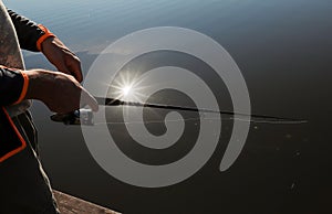 Male hands holding fishing rod closeup over river or lake with reflection of sun rays