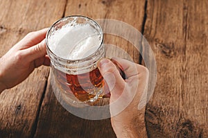 Male hands holding full glass of blonde beer.