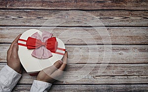 Male hands holding a heart shaped gift box with bow ties on wooden table with copy space