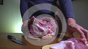 Male Hands Holding Knife and Cutting Meat on the Cutting Board. Cuts Fresh Meat Standing at Table in Domestic Kitchen in