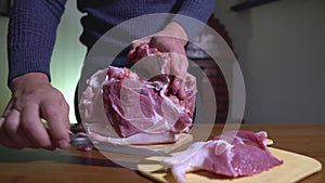 Male Hands Holding Knife and Cutting Meat on the Cutting Board. Cuts Fresh Meat Standing at Table in Domestic Kitchen in