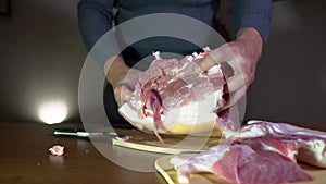 Male Hands Holding Knife and Cutting Meat on the Cutting Board. Cuts Fresh Meat Standing at Table in Domestic Kitchen in