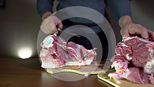 Male Hands Holding Knife and Cutting Meat on the Cutting Board. Cuts Fresh Meat Standing at Table in Domestic Kitchen in