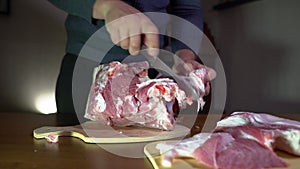 Male Hands Holding Knife and Cutting Meat on the Cutting Board. Cuts Fresh Meat Standing at Table in Domestic Kitchen in