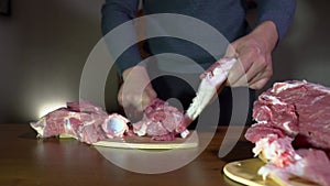 Male Hands Holding Knife and Cutting Meat on the Cutting Board. Cuts Fresh Meat Standing at Table in Domestic Kitchen in