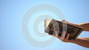 Male hands holding Koran on sky background, template for islamic inscriptions