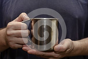 The male hands are holding a metal mug with a hot drink