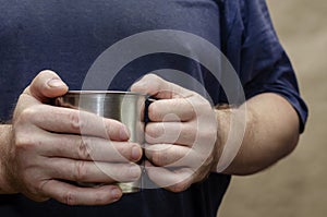 The male hands are holding a metal mug with a hot drink