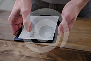 Male hands holding modern black e-book reader, digital book, tablet computer device for displaying text electronically, electronic