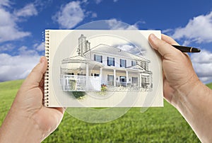 Male Hands Holding Paper With House Drawing Over Empty Grass Field