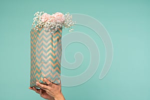 Male hands holding shopping bag with tender flowers,  over blue background with copyspace