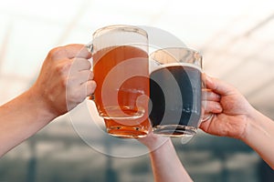 Male hands holding three glass mugs of light and dark draft beer. Beer toast, cheers