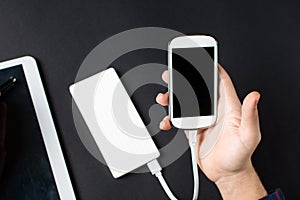 Male hands holding a white cellphone connected to a power bank