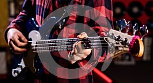 Male hands holds bass guitar, play music in club atmosphere background. Play guitar concept. Fingers clamp strings on