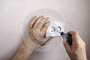 Male hands install and screw a white electrical outlet to the wall