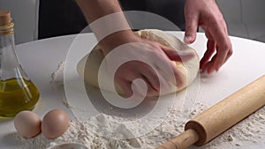 Male hands kneading dough for braed or pastry. Closeup shot of chef making pizza dough on table