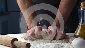 Male hands kneading dough with flour on kitchen table. Chef cooks dough in slow motion front view