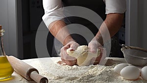 Male hands kneading dough with flour on kitchen table. Chef cooks dough in slow motion front view