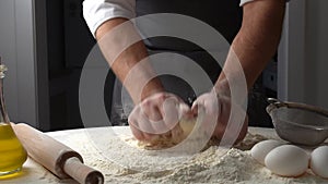 Male hands kneading dough with flour on kitchen table. Chef cooks dough in slow motion front view