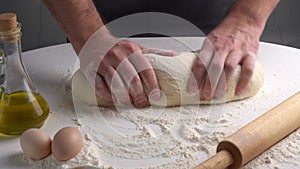 Male hands kneading dough with flour on kitchen table. Chef cooks dough in slow motion front view