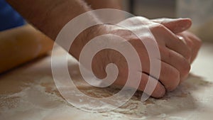 Male hands kneading dough in flour on table.