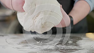 Male hands kneading raw dough on metal kitchen table covered with flour. Unrecognizable Caucasian pizza chef cooking